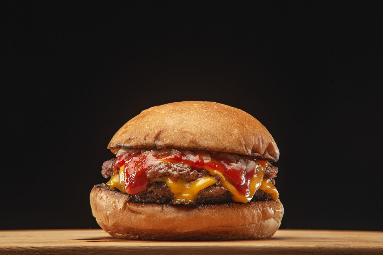 Delicious cheeseburger with melted cheese and ketchup on a black background, highlighting food presentation.