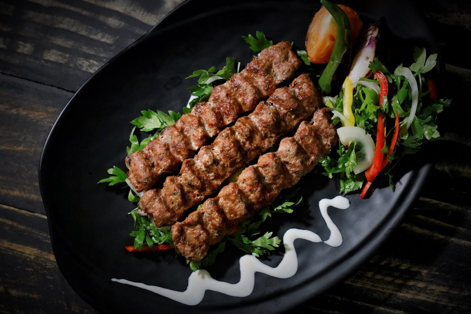 Succulent grilled kebab served with fresh salad on a black plate. Perfect for food lovers.